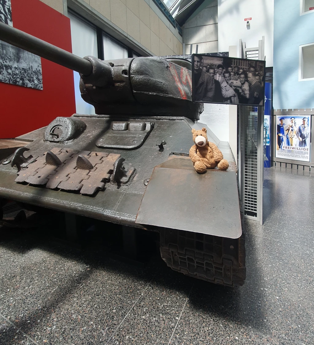 Der kleine Bär sitzt auf einem Panzer.